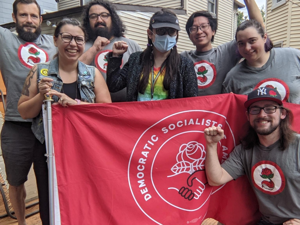 People standing with fists up in front of DSA flag smiling